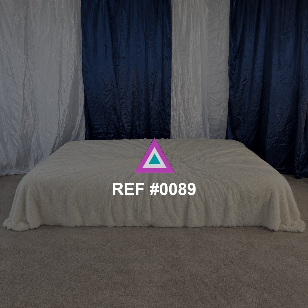 Refugio de Pliegues. Una cama baja de tela marfil frente a cortinas azules y blancas.
