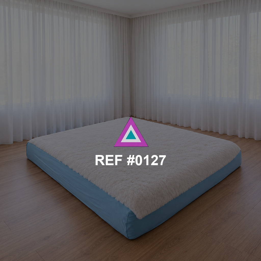 Sueño a Ras del Suelo. Una cama baja de base azul y ropa blanca en un interior de grandes cortinas claras.