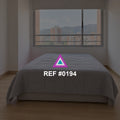Ciudad en Reposo. Una cama gris junto a una ventana amplia que muestra edificios de la ciudad.