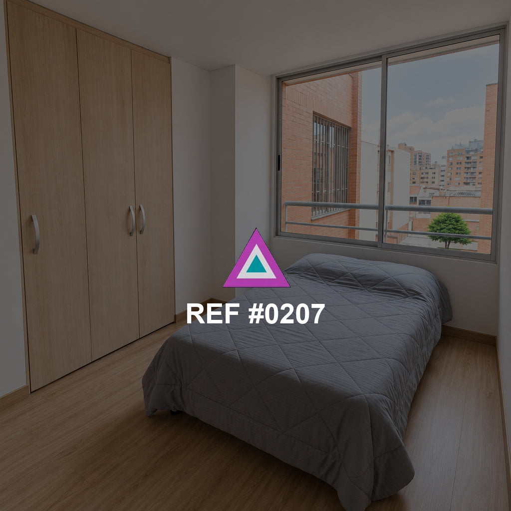 Ventana al Barrio. Una cama gris junto a un armario de madera y una ventana hacia edificios de ladrillo.