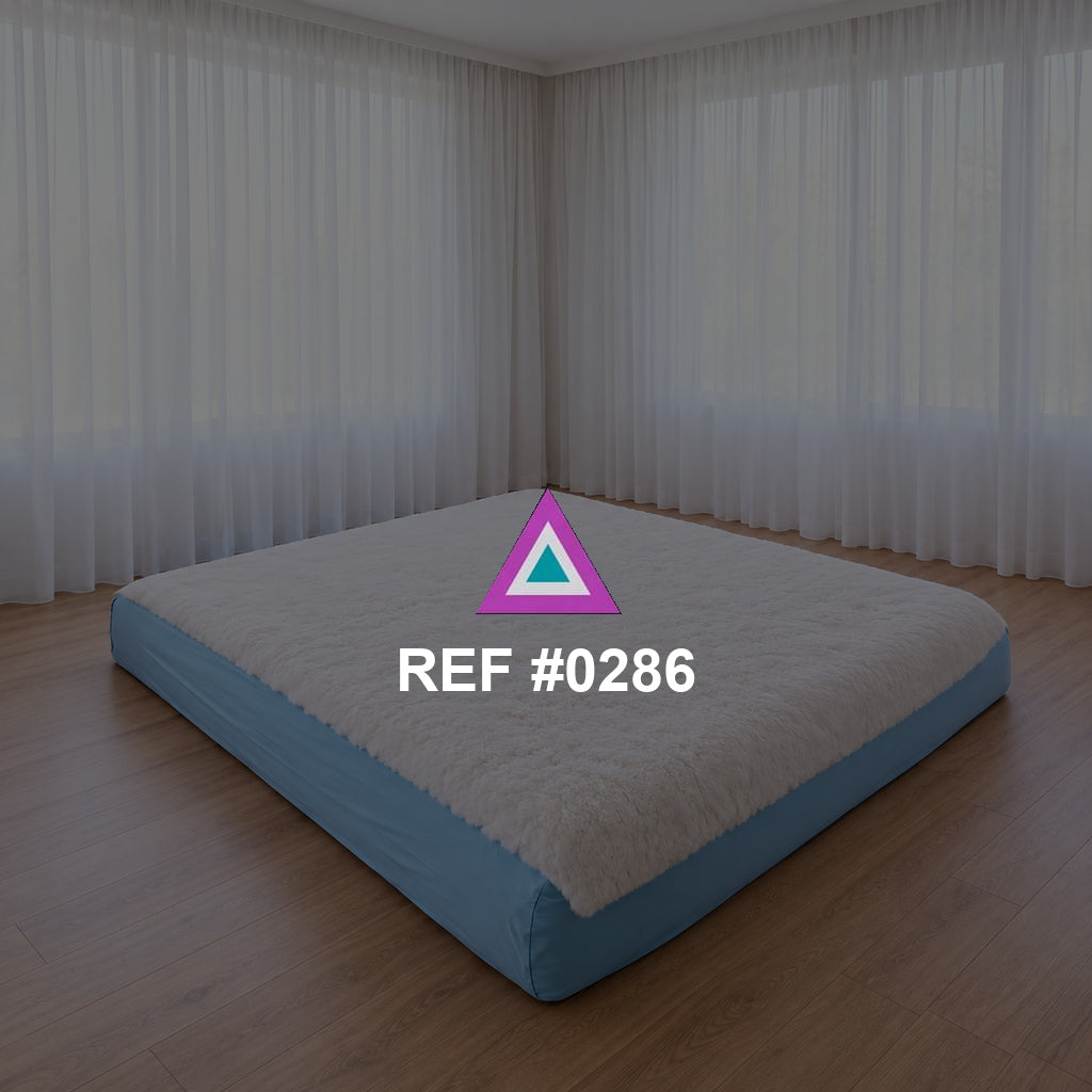 Sueño a Ras del Suelo. Una cama baja de base azul y ropa blanca en un interior de grandes cortinas claras.