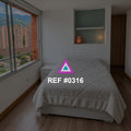 Ventana de Olivo. Una cama gris junto a una ventana urbana y un nicho de tono verde suave.